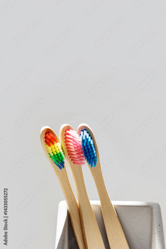 Eco friendly Bamboo toothbrushes with colored bristles in square shaped grey concrete toothbrush holder at sunlight with shadows from window. Sustainable living concepts, minimal style aesthetic photo