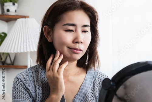 asian woman struggling with bell's palsy or facial palsy, showing facial weakness and a drooping mouth, holding her face while checking in the mirror, possibly caused by viral infections or stress