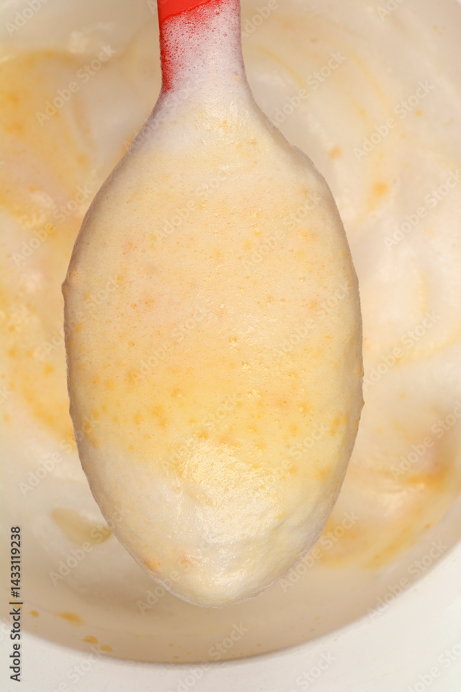 A red pastic spoon lifts a spoonful of light and airy biscuit batter, showing its bubbly texture