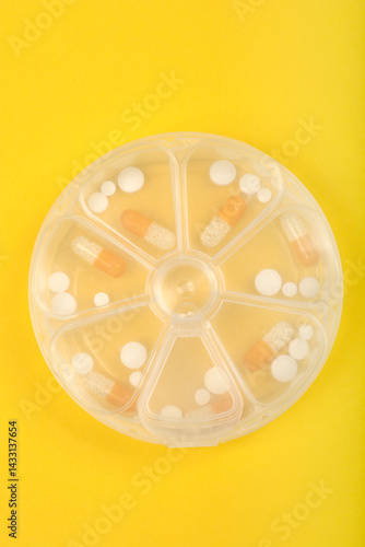 Obraz na płótnie A clear, round pill organizer with seven compartments holds various white and orange capsules and tablets against a bright yellow background w salonie