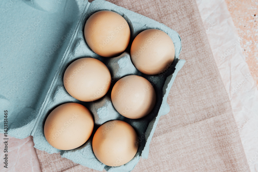 Brown chicken eggs in a blue carton box on light blue background, top view