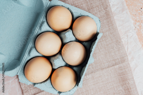 Brown chicken eggs in a blue carton box on light blue background, top view
