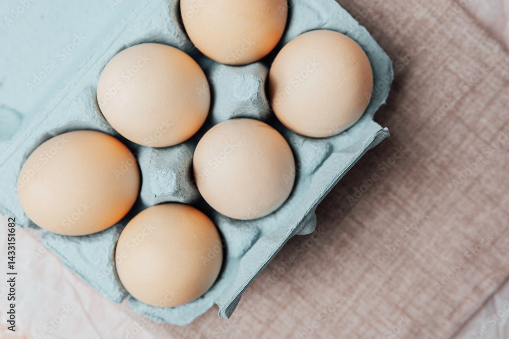 Brown chicken eggs in a blue carton box on light blue background, top view
