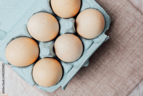 Obraz na płótnie Brown chicken eggs in a blue carton box on light blue background, top view w salonie