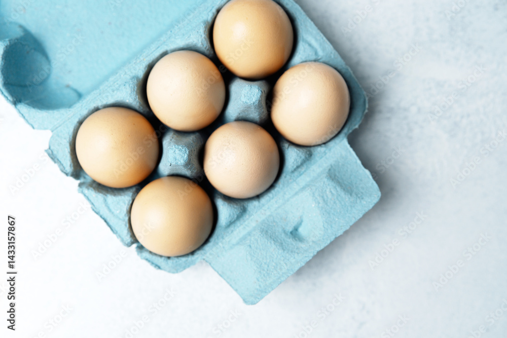 Brown chicken eggs in a blue carton box on light blue background, top view