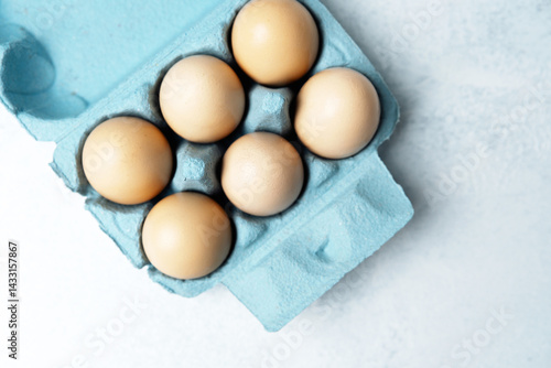 Obraz na płótnie Brown chicken eggs in a blue carton box on light blue background, top view w salonie