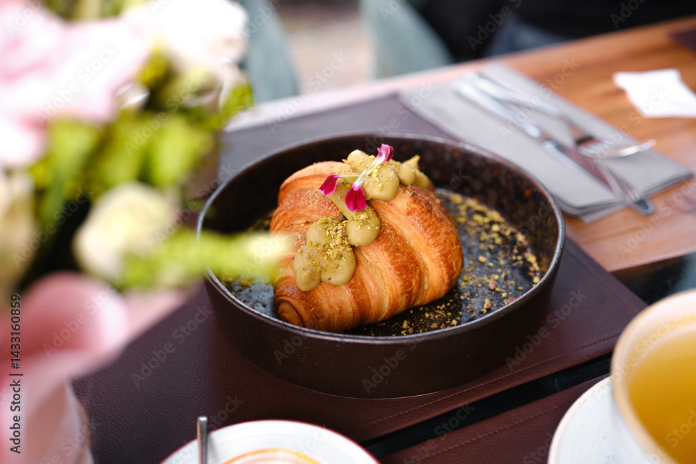 Delicious croissant topped with pistachio cream and edible flowers on a table