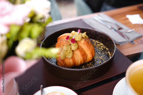 Obraz na płótnie Delicious croissant topped with pistachio cream and edible flowers on a table w salonie