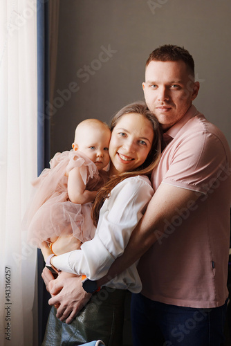 Obraz na płótnie Happy and gentle parents hold baby daughter in pink dress in their arms. w salonie