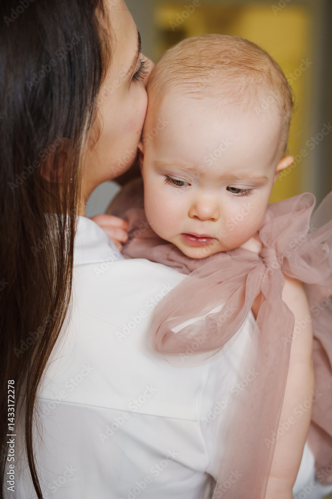 Cute baby daughter in an elegant dress lies on her mother's shoulder