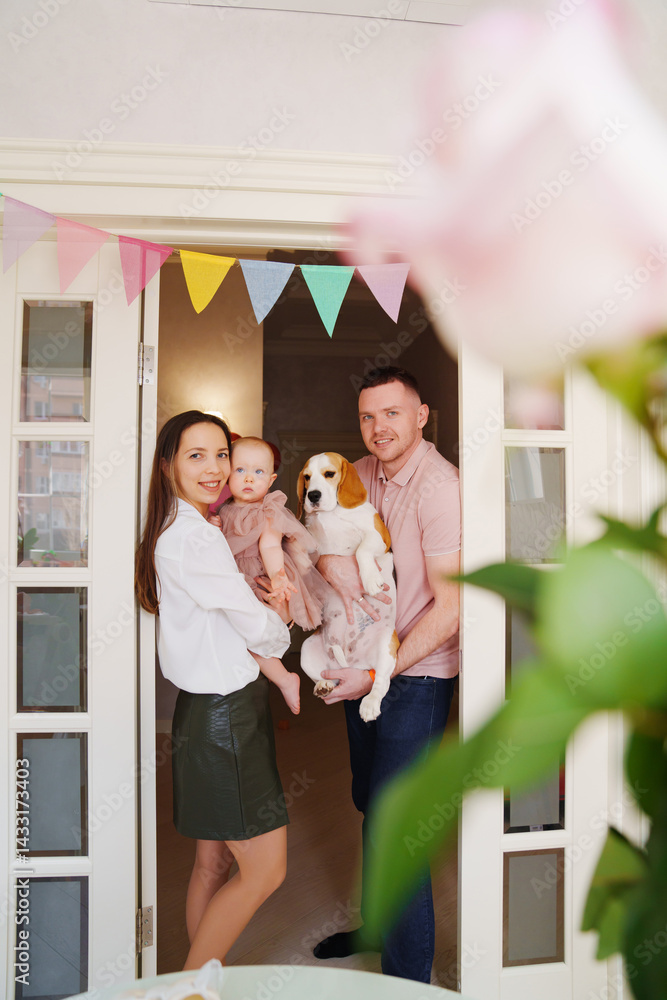 parents hold baby daughter in the doorway with a garland of colorful flags.