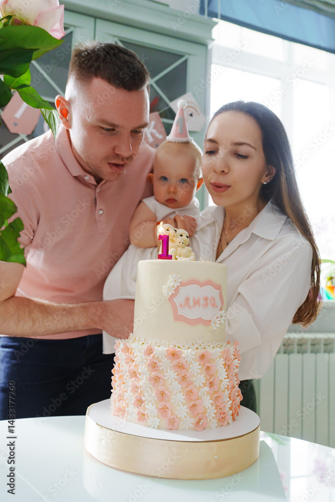 Mom and dad hold little daughter by the birthday cake.