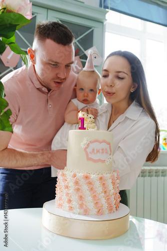 Mom and dad hold little daughter by the birthday cake. 