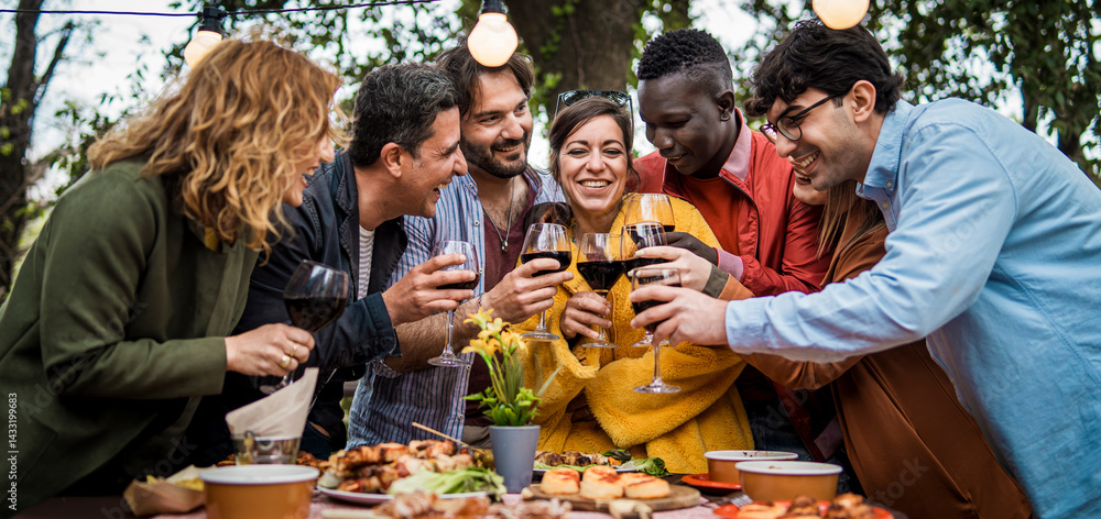 Obraz premium Happy diverse friends toasting at festive outdoor dinner with wine and lights