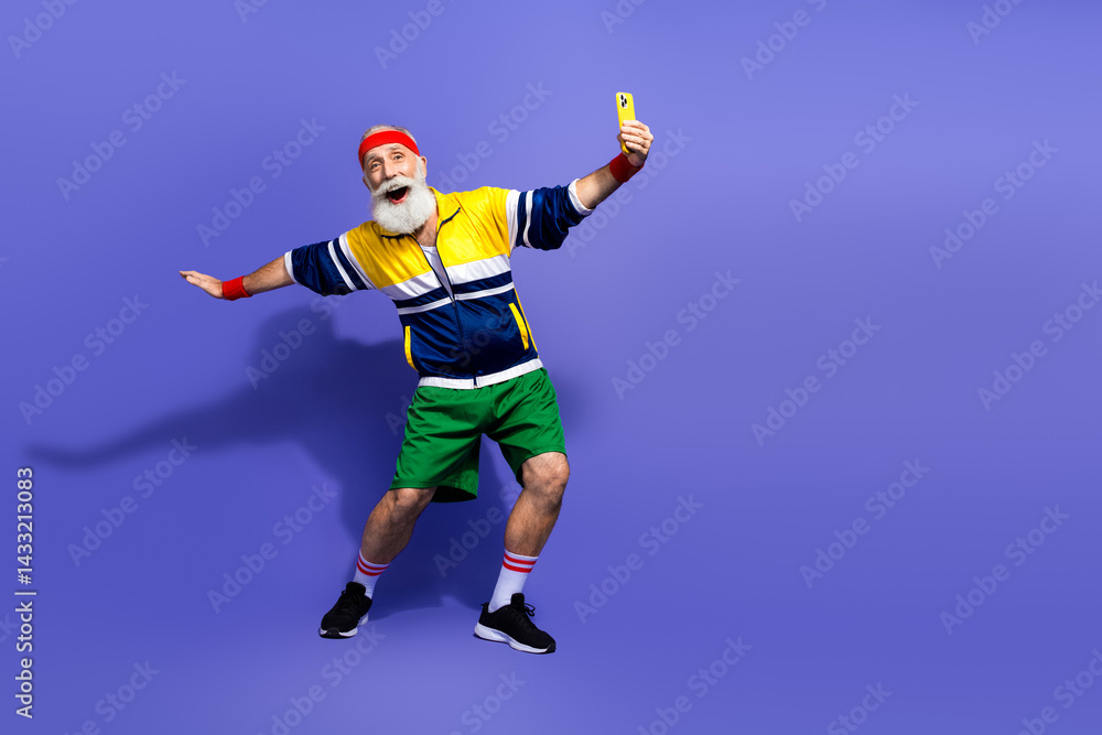 Obraz premium Elderly man dressed in vibrant retro sportswear posing energetically on a purple background