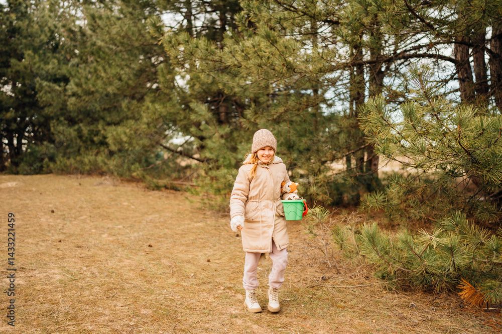 A little girl collects cones in a plastic baby bucket