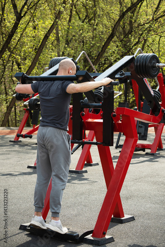 Male athlete engages in outdoor strength training using a leg press machine with weights. Man demonstrates determination during his workout. Open air.