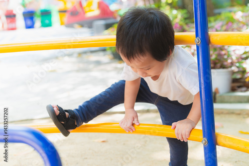 Child's Playful Climb concept. Asian young child concentrates with a determined expression as he explores a vibrant playground. Baby boy 2.5 years old.