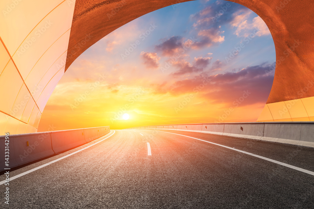 Empty road leading through an arch towards a bright sunset