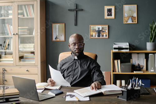 Billede på lærred African American pastor in black cassock sitting in comfortable leather chair wh