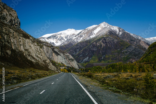 Obraz na płótnie A mountain road winding through the rugged terrain of the Altai Republic, surrounded by harsh, snow-covered peaks and dramatic natural beauty. w salonie