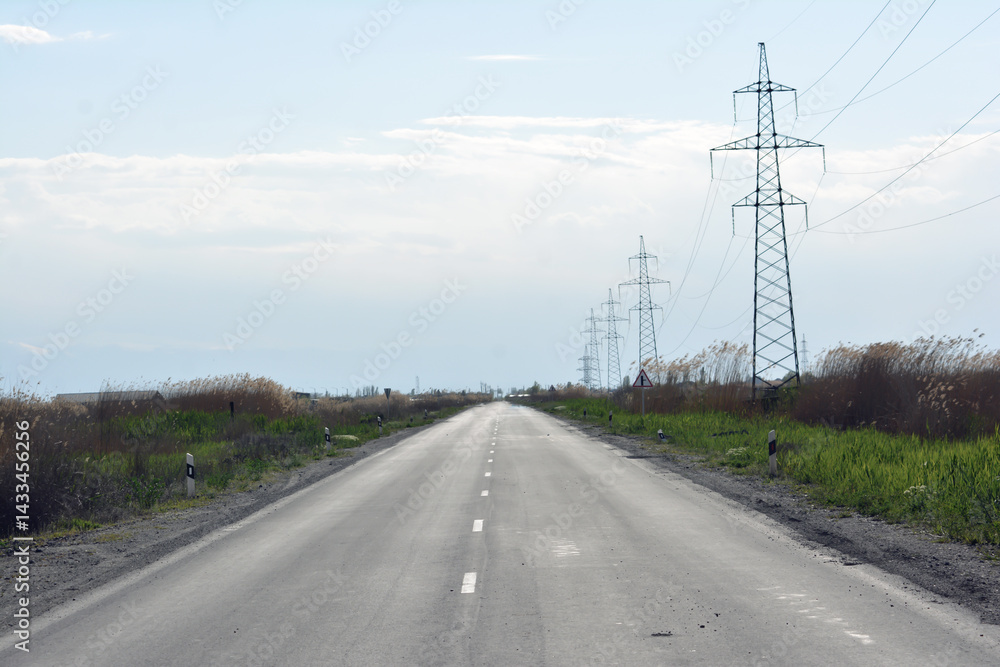 Fototapeta premium High-voltage power lines on the road in the mountains. Road and electric powers
