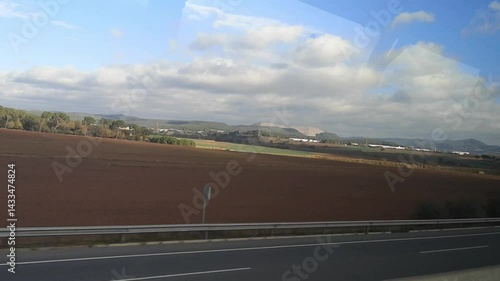 Bus ride video through Catalonia, Spain, showcases vast fields and hills under a clear sky. Video 38 sec. Gentle sunlight and passing cars highlight the serene, rural landscape of a tranquil journey