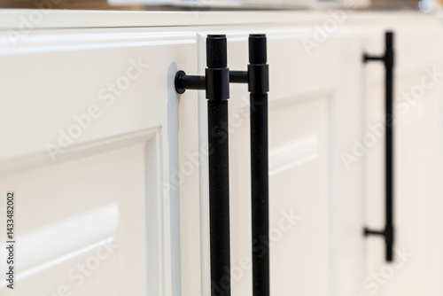 Modern black kitchen cabinet handles on white doors  Close-up of sleek black metal handles with knurled texture on glossy white kitchen cabinet doors, showcasing contemporary interior design detail