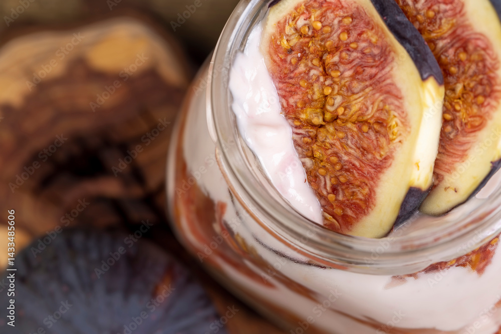 fresh pink yogurt with fig flavor in a glass jar and with red figs cut into pieces, closeup
