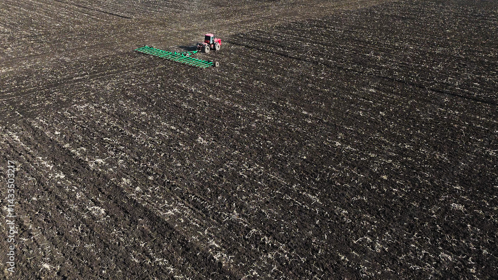 Obraz premium A red tractor works on a plowed field in spring, Russia farming