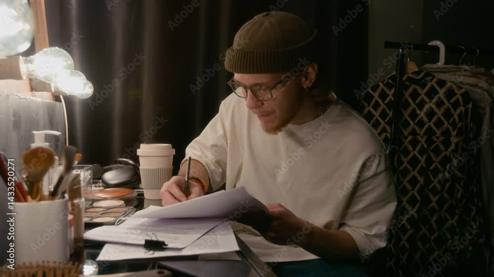 Young man reading his stand-up script out loud and making notes and changes while sitting in dimly lit dressing room Young man reading his stand-up script out loud and making notes and changes while sitting in dimly lit dressing room