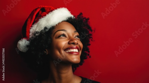African-American woman smiles, looks up, wearing Santa hat, exudes joy, celebrates holiday season.