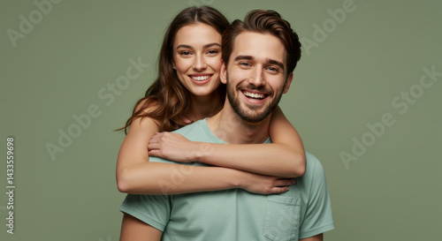 Young couple embracing in soft sage green clothing against a plain backdrop. Smiling and affectionate pose in a studio setting.