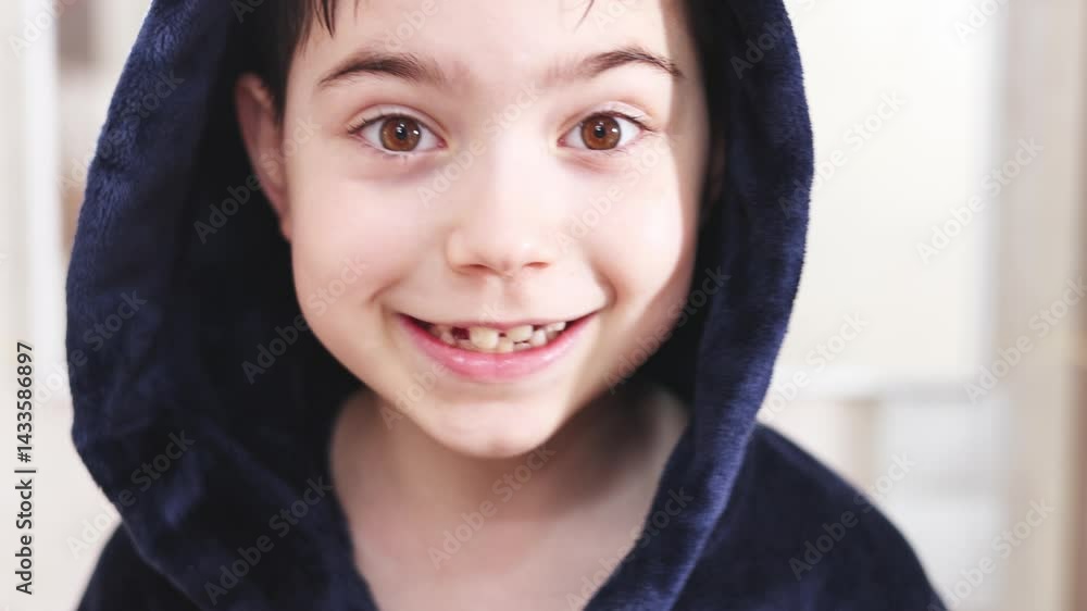 kid in bathroom in bathrobe looking in mirror and smiling. boy combing wet fresh washed hair.preschooler boy with front permanent teeth in rising.daily routine hygiene. child with hood on head. kid in bathroom in bathrobe looking in mirror and smiling. boy combing wet fresh washed hair.preschooler boy with front permanent teeth in rising.daily routine hygiene. child with hood on head.