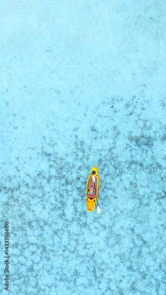 Obraz premium woman in a bikini relaxes on a yellow kayak floating on clear turquoise sea, top-down view from above, peaceful moment in tropical paradise, summer holiday, maldives, travel, holidays, vacation