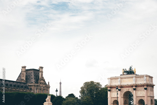View of the Arc de Triomphe du Carrousel with its quadriga sculpture, framed by the Louvre buildings, with the Eiffel Tower visible far behind.