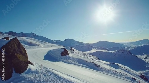Snowy mountain slopes under bright sun.  Vast expanse of pristine white snow-covered landscape with rocky outcrops.  Ski trail winds through the terrain