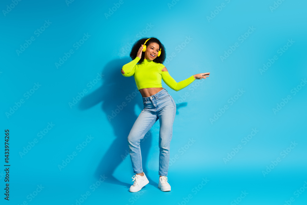 Young woman dancing joyfully wearing neon green top and jeans against vibrant blue background Young woman dancing joyfully wearing neon green top and jeans against vibrant blue background