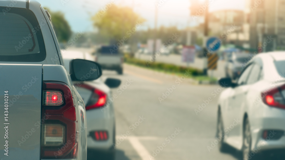 Fototapeta premium Rear side of pickup car white color. Turn on brake light. Cars are stopped at traffic lights at intersections. Background of trees side and green grass center of road.