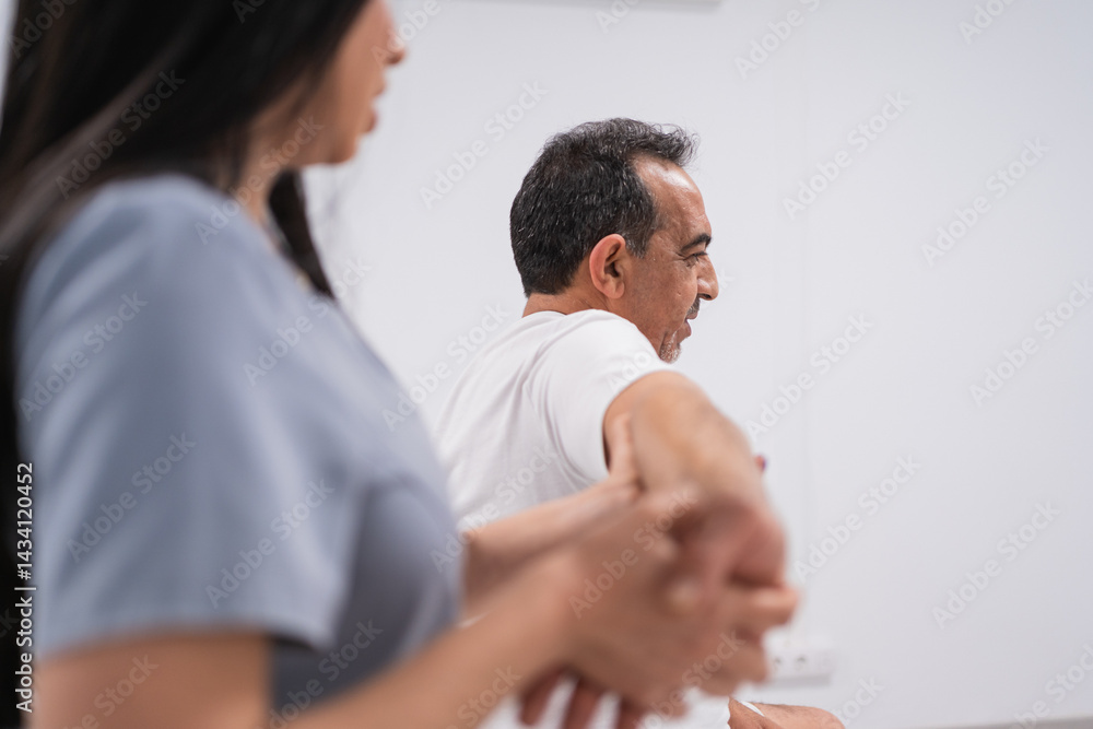 Physiotherapist assisting mature man stretching arm during physiotherapy session in medical clinic Physiotherapist assisting mature man stretching arm during physiotherapy session in medical clinic