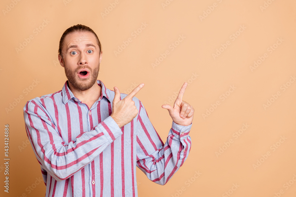 Surprised young man in a striped shirt gesturing with raised hands against a beige background Surprised young man in a striped shirt gesturing with raised hands against a beige background