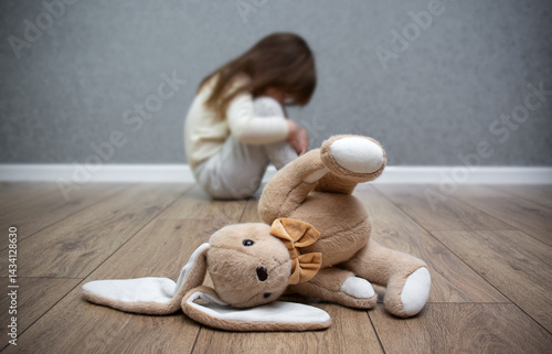 A stuffed bunny on the floor, a scared child sitting behind it. Child abuse. Bullying in the family.