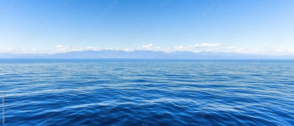 Obraz premium Serene seascape featuring gentle ocean waves under a clear blue sky with distant mountain range offering a tranquil and calming visual experience for viewers