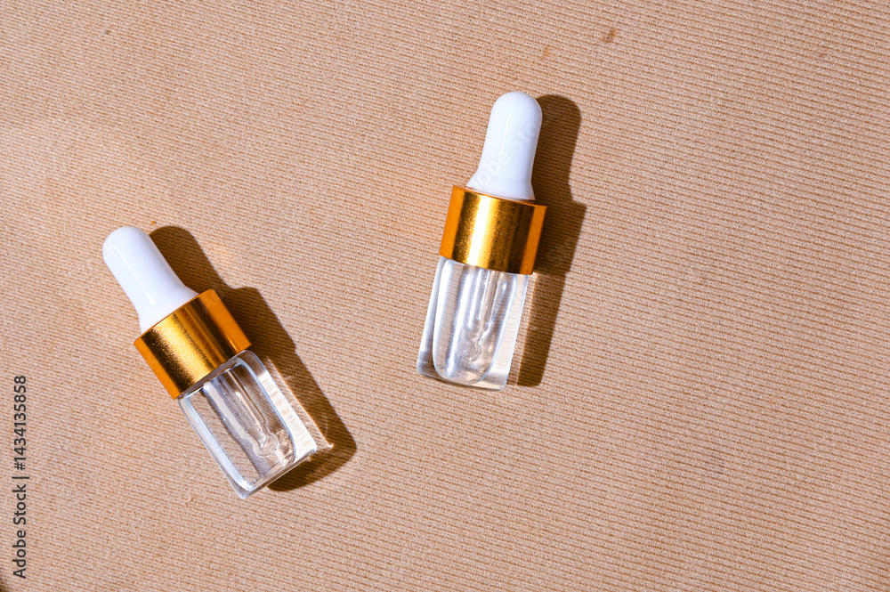 Two transparent serum dropper bottles with golden caps placed on textured beige background, surrounded by fresh lemon slices. Clean, elegant skincare flat lay for beauty and citrus-themed ads