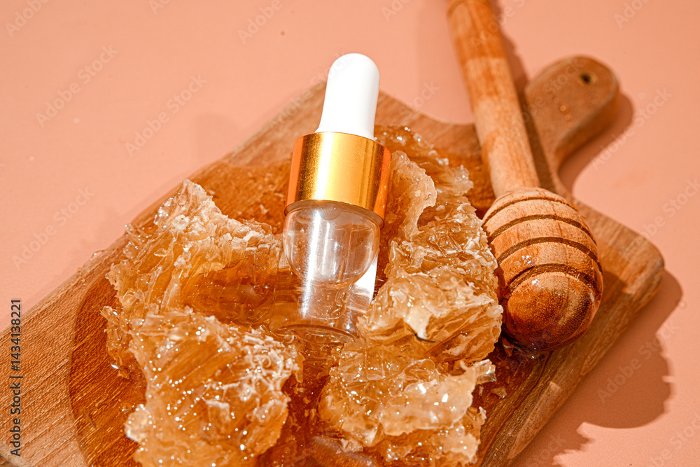 Amber glass serum dropper bottle placed on honeycomb chunks and wooden dipper on cutting board, with peach background. Natural skincare product concept featuring honey as key organic ingredient