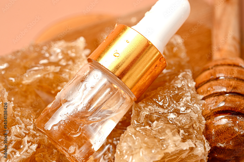 Amber glass serum dropper bottle placed on honeycomb chunks and wooden dipper on cutting board, with peach background. Natural skincare product concept featuring honey as key organic ingredient