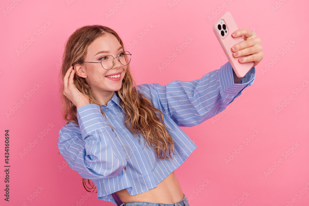 Smiling young woman in a striped blue blouse taking a selfie on a vibrant pink background, expressing joy and confidence
