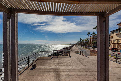 Sea of ​​Cortes, promenade and vehicular road with palm trees in central median, buildings and house in background, view from coastal lookout, sunny afternoon in Loreto in Baja California Sur, Mexico