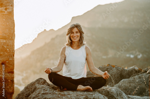 Foto Yoga teacher seated cross-legged at sunset in the mountains