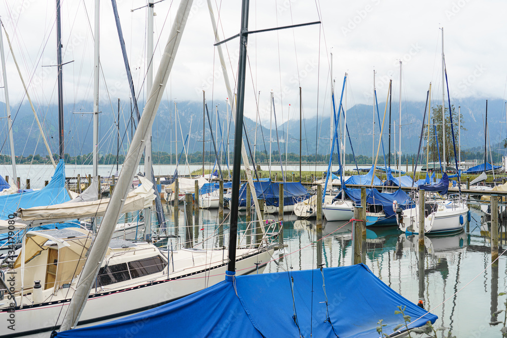 Fototapeta premium Sailboats anchored at a marina under cloudy skies with mountains in the background near a waterway